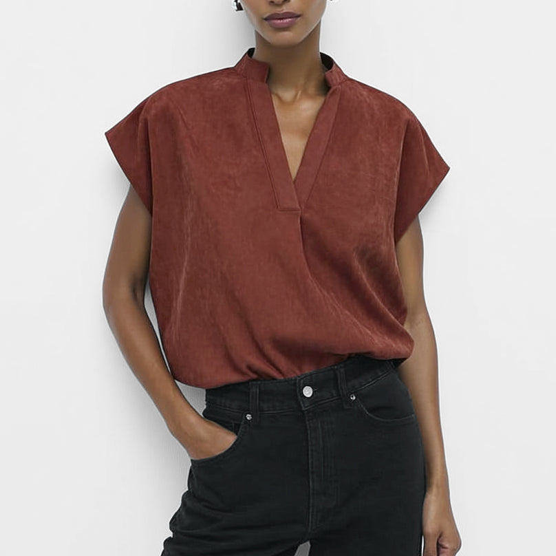 Woman wearing a rust-colored top and black pants against a white background
