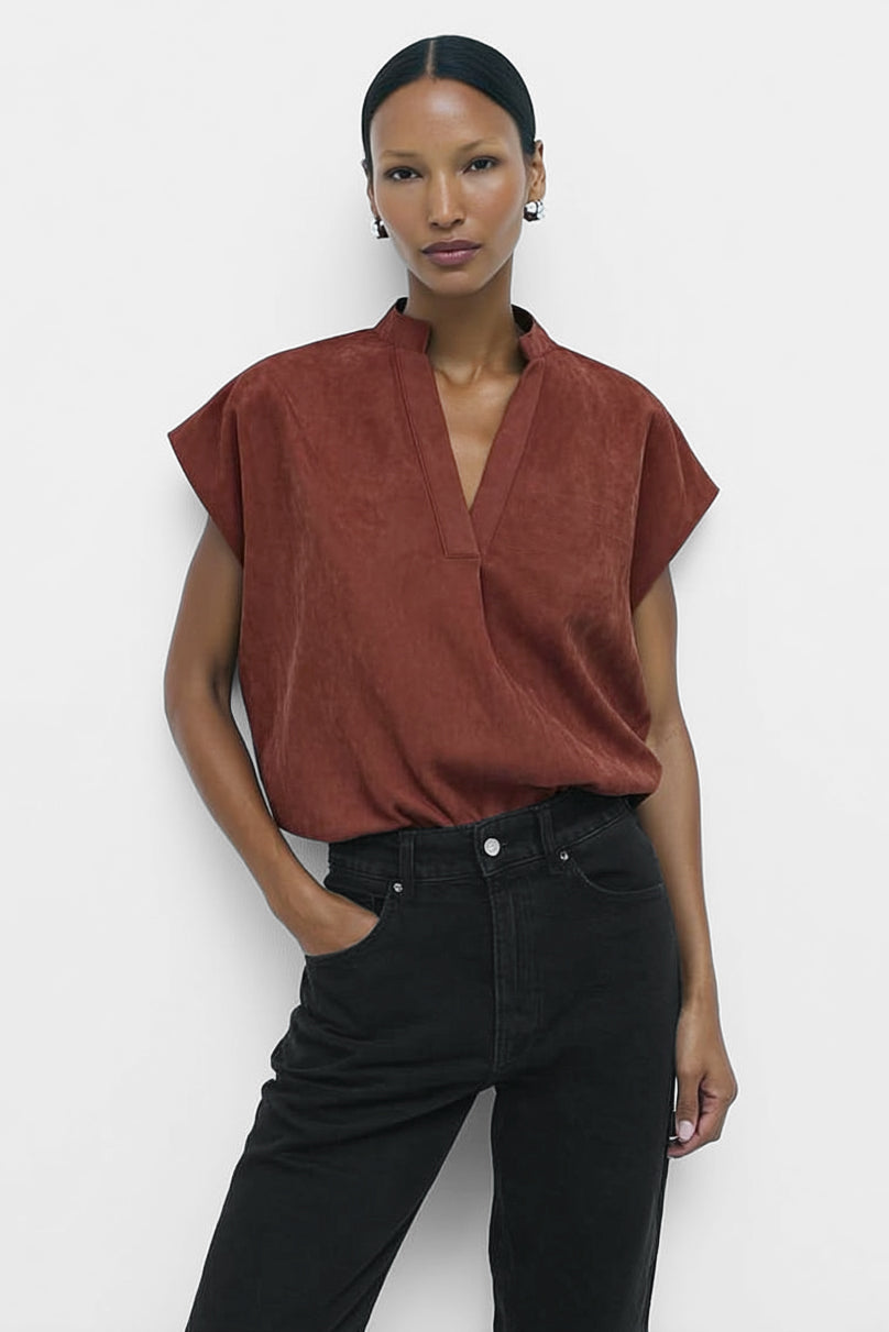 Woman wearing a rust-colored top and black pants against a white background