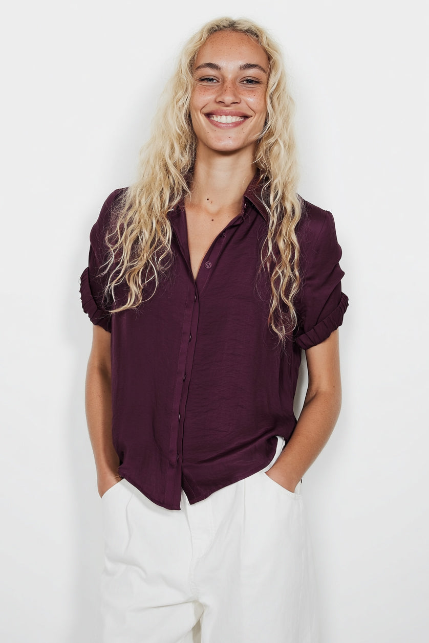 Woman wearing a dark purple shirt and white pants against a plain background