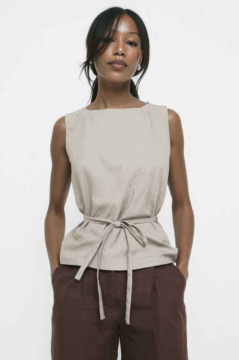 Woman wearing a beige sleeveless top with a tie waist and brown pants on a white background
