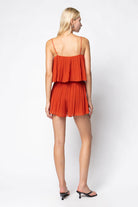 Woman wearing an orange pleated romper on a white background