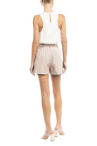 Woman wearing a white sleeveless top and beige pinstripe shorts on a white background