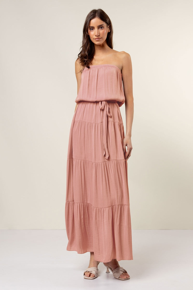 Woman wearing a pink strapless dress with a tiered skirt on a white background