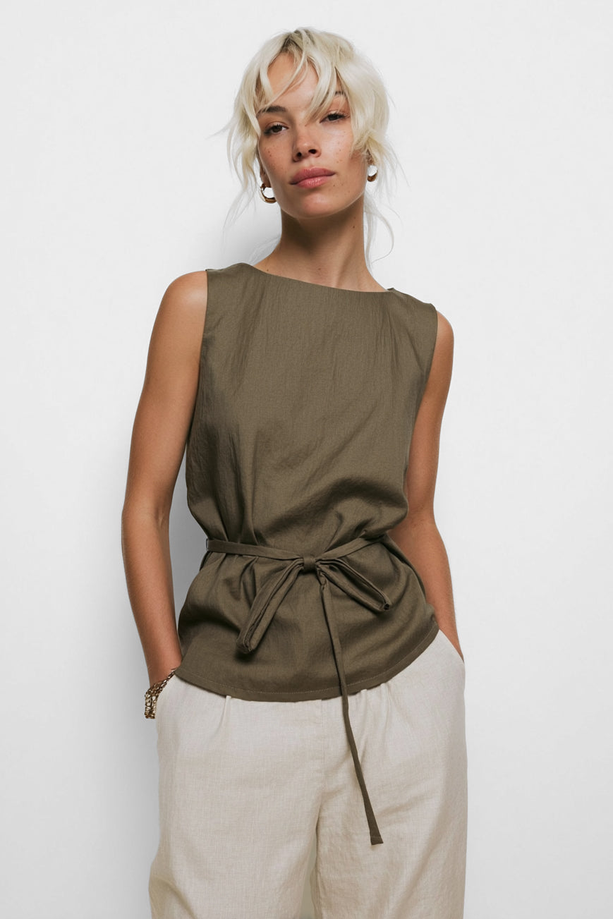 Woman wearing an olive green sleeveless top with a tie waist against a white background